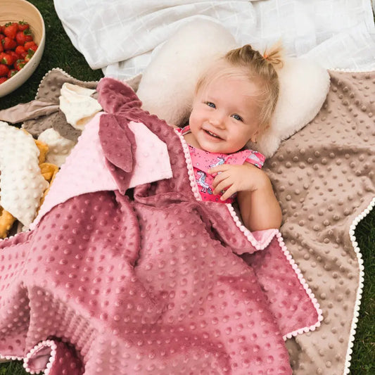 A baby lies on a plush 2in1 Blanket with Baby Comforter in Dusty Rose, featuring a Milky fabric side for warmth and a satin side for cooling, adorned with textured bubbles for sensory stimulation.