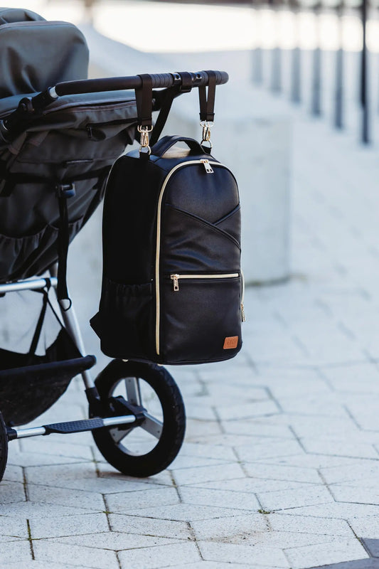 A black backpack with stroller straps, featuring 16 pockets, laptop and baby food compartments, and a waterproof changing mat. Designed in Europe with vegan leather and YKK zippers for stylish, organized parenting on the go.
