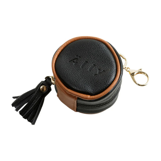 A black and brown round pacifier bag with a tassel, key chain, and zipper. Designed for storing pacifiers and essentials, attaches to bags and strollers. Dimensions: 7x7x5 cm.