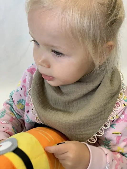 A child holding a handmade double-sided muslin scarf-bib in khaki, designed for style and comfort. Soft and practical, suitable for ages 6 months to 3 years.