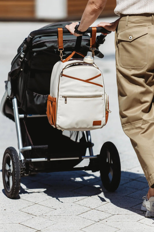 A person pushing a stroller with a Cappuccino Diaper Bag, featuring multiple pockets, thermal lining, and stroller straps for hands-free convenience. Stylish, organized, and versatile for parents on the go.