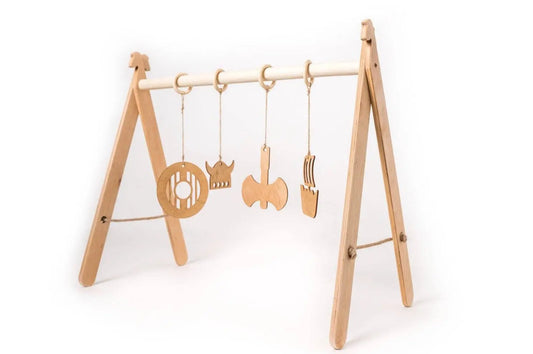 A wooden play gym for babies featuring Viking-themed hanging toys on a sturdy frame. Promotes muscle development and coordination. Dimensions: 65 x 59 x 31 cm. Made in Europe.