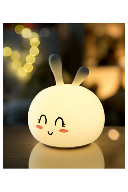 A white Bunny Silicone Lamp with a friendly face and ears, soft to touch, lighting in 7 colors, and safe for children. Dimensions: 14.1 x 11.6 x 11.6 cm.