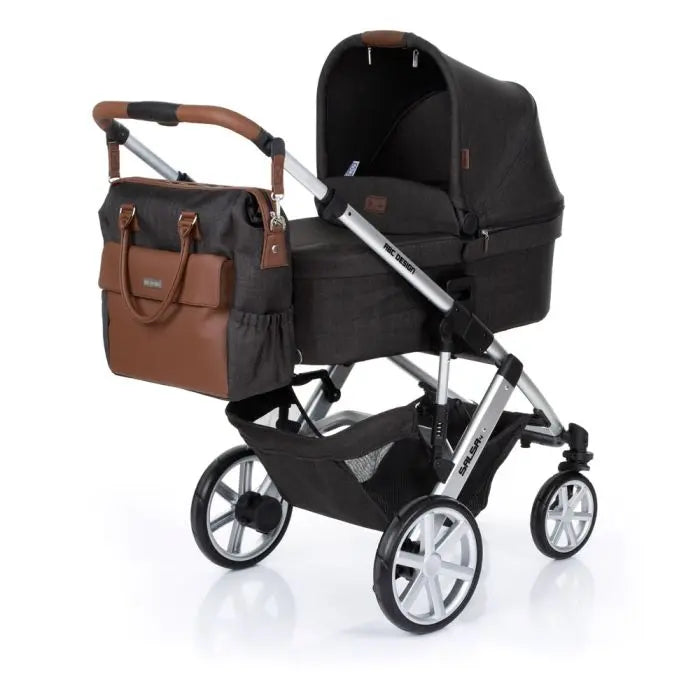 A black and brown Jetset Diaper Bag by ABC Design, showcasing spacious design, practical organization, durable construction, and versatile carrying options for busy parents on the go.