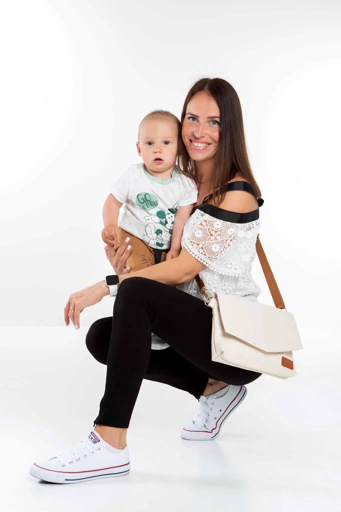 A woman holding a baby, showcasing the Baby Accessories Handbag – Cappuccino. Versatile design with long and wrist straps for hands-free carrying. Lightweight, durable materials for convenience and style.