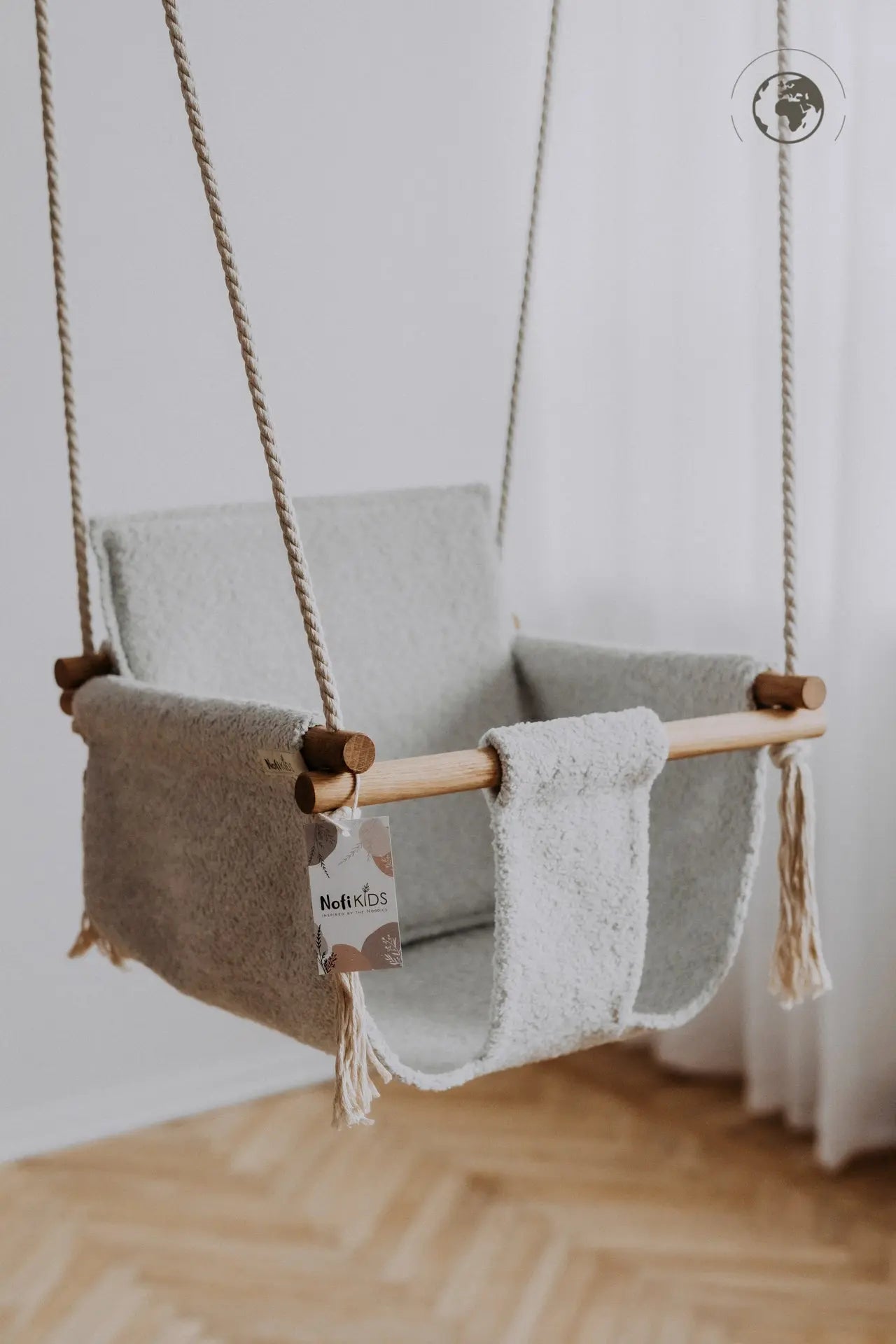 A white baby swing made from recycled materials, featuring oak wood poles and a removable bouclé fabric in Ice Grey. Safe, durable, and stylish for indoor use.