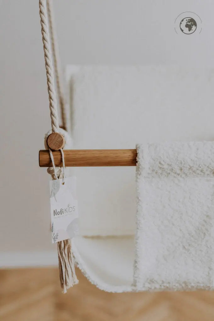 A luxurious Baby Swing in Bouclé Snow White, crafted from recycled materials with oak wood poles, pillow, and carabiners. Safe, stylish, and eco-friendly for indoor use.