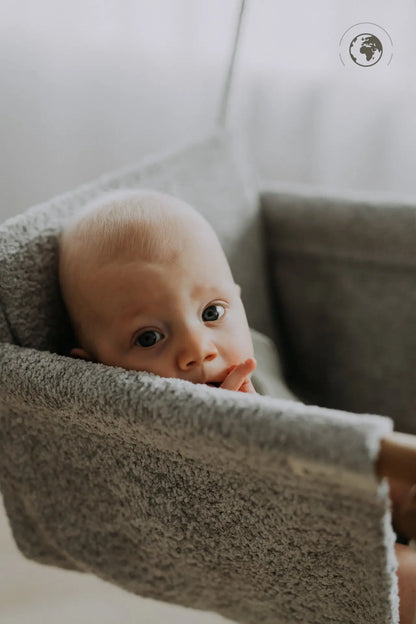 A baby swing in Bouclé Stone Grey, made from recycled materials and oak wood poles, ensuring safety and comfort. Certified quality swing with removable, washable fabric and Nordic design.