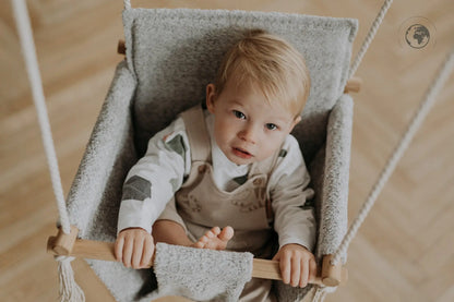 A toddler in a luxurious baby swing made from recycled materials, featuring cozy bouclé cloth and oak wood poles. Safe, stylish, and eco-friendly.