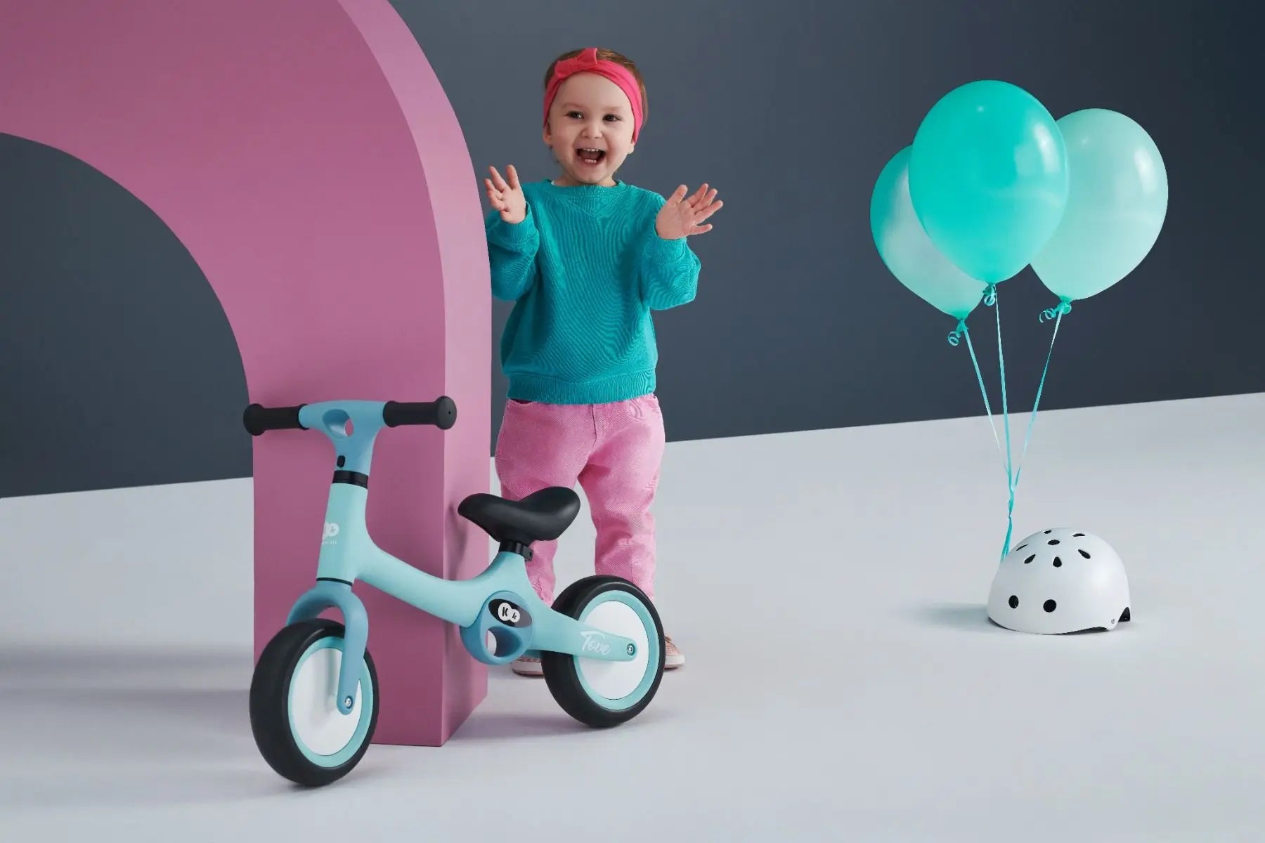 A child next to a mint TOVE balance bike with puncture-resistant wheels, adjustable seat, and two carry handles for easy transport.