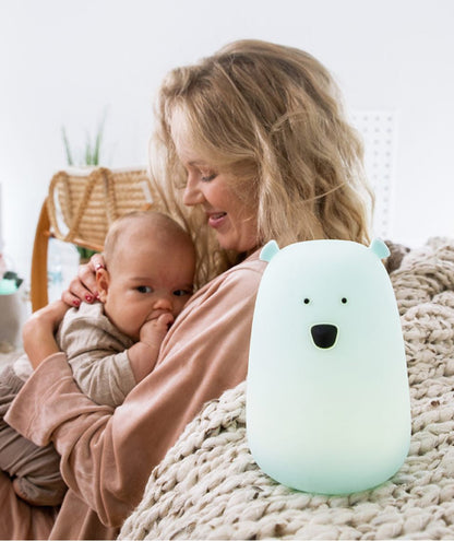 A woman holding a baby, a white object with a face, and a baby in a woman's arms. Big Bear Silicone Lamp with Remote - Blue, soft, touch-responsive, 7-color glow, remote-controlled, safe for children.