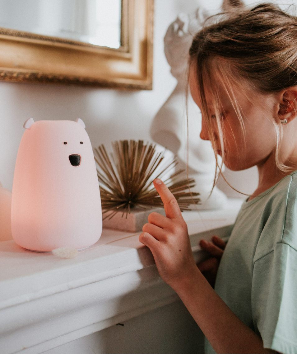 A girl pointing at a pink teddy bear lamp with remote control, soft silicone material, multifunctional features, and child-friendly design.