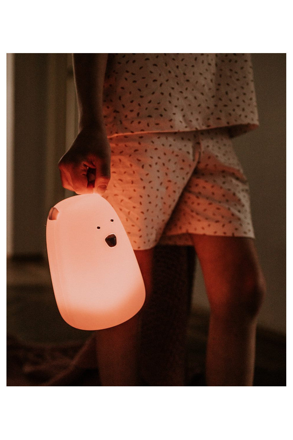 A person holding a pink teddy bear lamp with remote control, featuring soft silicone material, gentle light, and multifunctional settings for a cozy, safe ambiance.