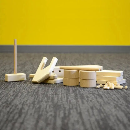 A group of wooden objects on the floor, including a wooden truck with a hole in it, surrounded by a yellow pole and a carpet. Experience the joy of creating and playing with our DIY Wooden Truck set, engaging children and parents in craftsmanship and creativity.