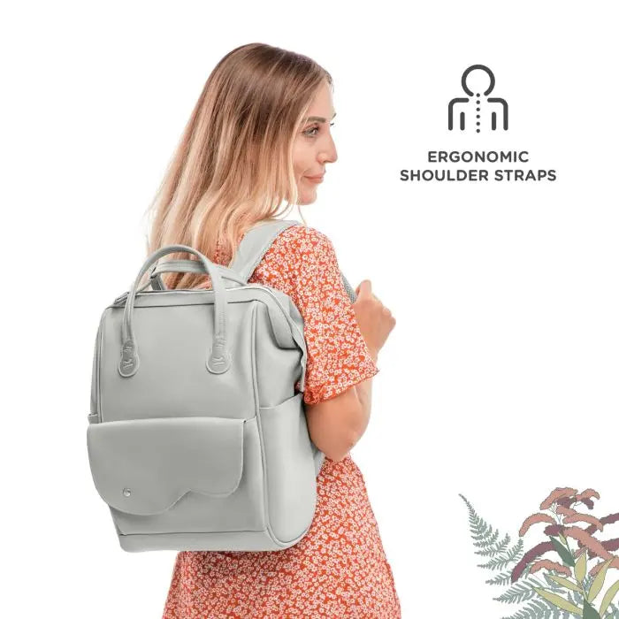 A woman wearing a red dress and a white backpack, featuring the Diaper Backpack Treasureback from the Nature Vibes collection, designed for organized outings with 9 practical pockets and stroller attachment capability.