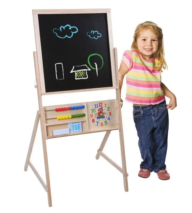 A girl stands by a Double Face Board, featuring a clock and blackboard. Encourage creativity with this double-sided chalkboard for kids, complete with chalk and eraser. Dimensions: 110 x 58 x 54 cm.