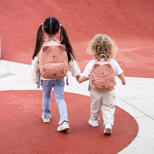 Two girls holding hands, one wearing Backpack - Mrs Cat, a pink backpack with cat face. Child holding hands with backpack, person carrying it.