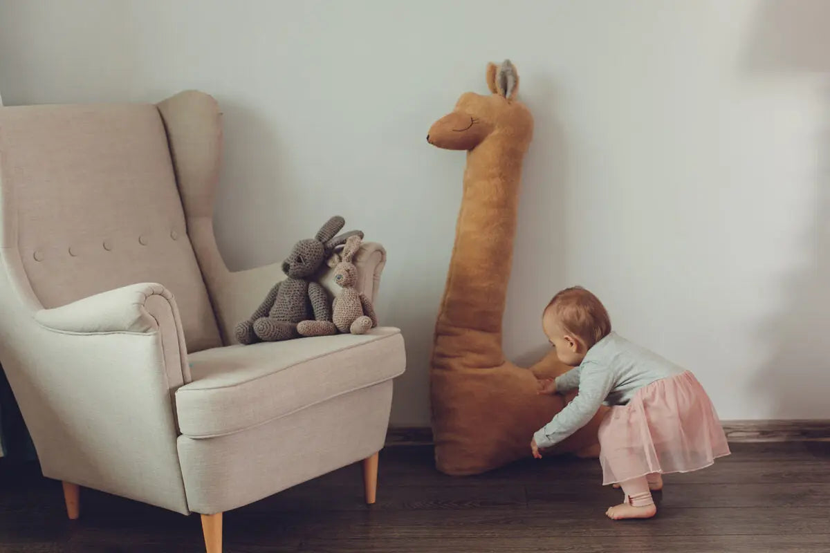 A baby interacts with a Giant Plush Toy Alpaca in Rust, handmade with super soft vegan fur. Versatile as a pillow or playmate, this oversized alpaca exudes whimsical charm and cozy comfort.