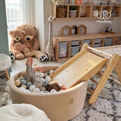 A child playing in a ball pit with a couple of teddy bears, a giraffe, and a wooden slide in the background. Teddy bear product - Giant Teddy 200 cm, soft fur, EU safety certified, washable, made in Europe.