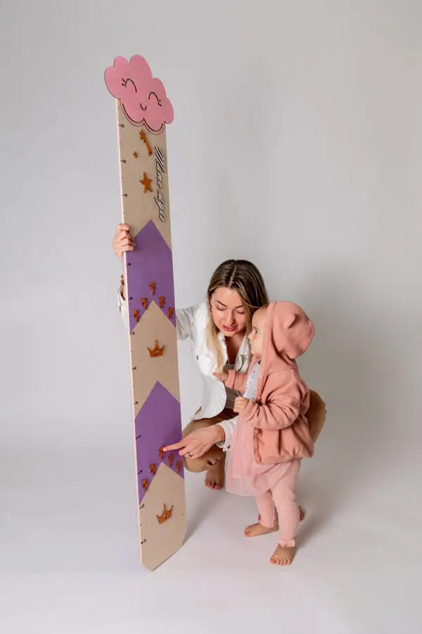 A woman and child hold a large ruler, a baby blue growth chart with clouds and raindrops, a charming way to track child's growth.