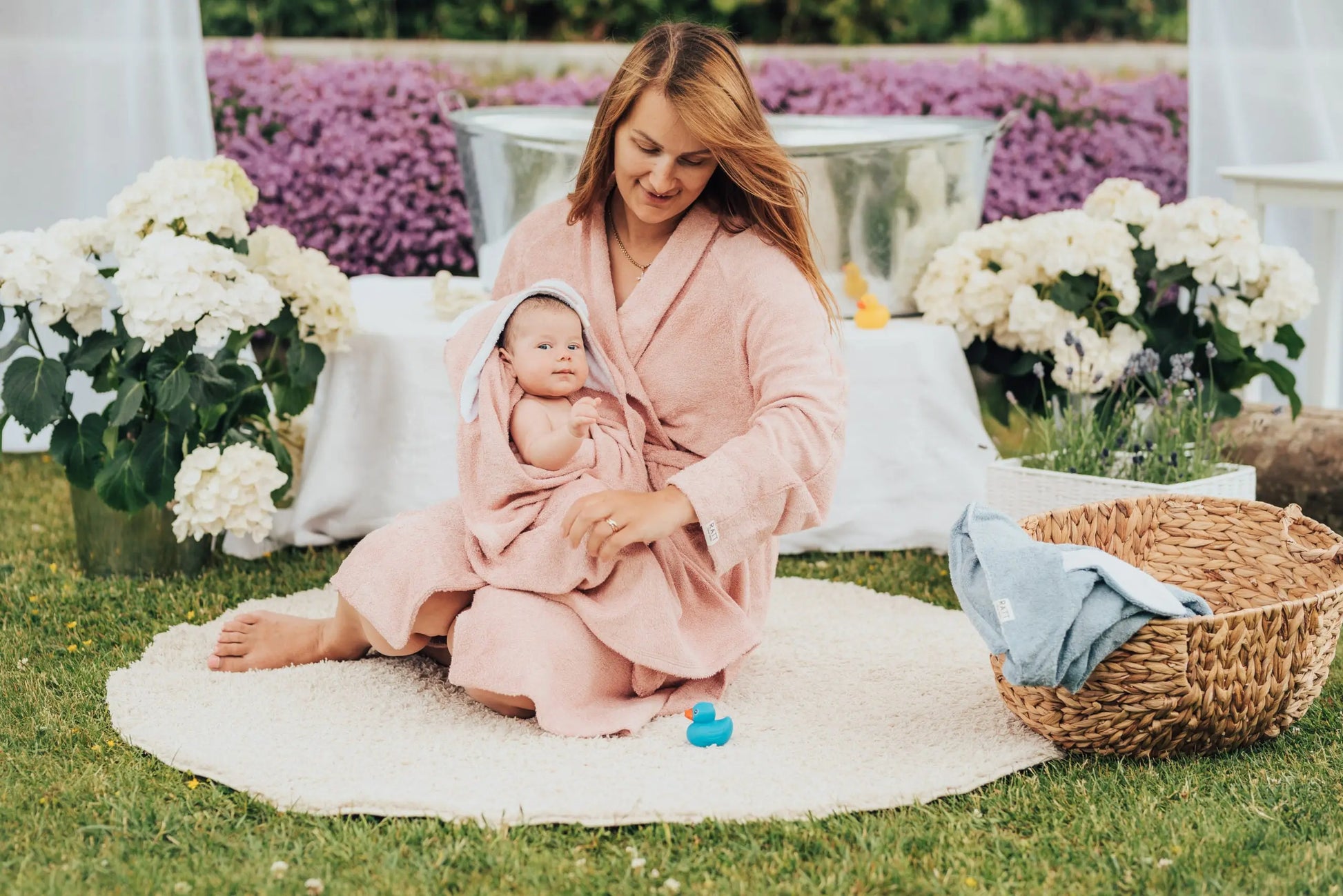 A woman in a bathrobe holding a baby wrapped in a Hooded Baby Bath Towel with RABBIT ears, made from bamboo terry for gentle care on delicate skin.