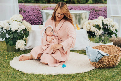 A woman in a bathrobe holds a baby wrapped in the Hooded Baby Bath Towel TEDDY with cute teddy ears, perfect for keeping infants warm and cozy post-bath. OEKO-TEX certified bamboo terry material.