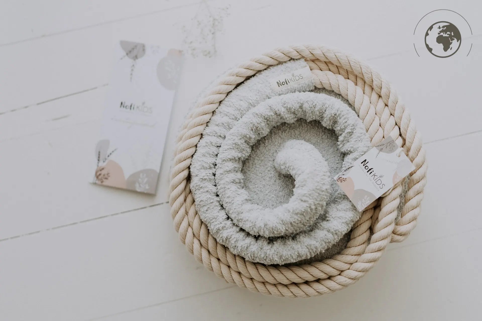 A white towel rolled up in a rope basket, representing the HopOn Swing - Bouclé Ice Grey, a safe and joyful swing for children with OEKO-TEX certified materials.