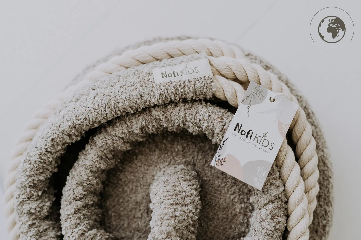 Close-up of HopOn Swing - Bouclé Sand with cotton rope, white tag, and earth logo. Supports physical development, OEKO-TEX certified materials, 100 kg load capacity. Designed in Europe for ages 3+.