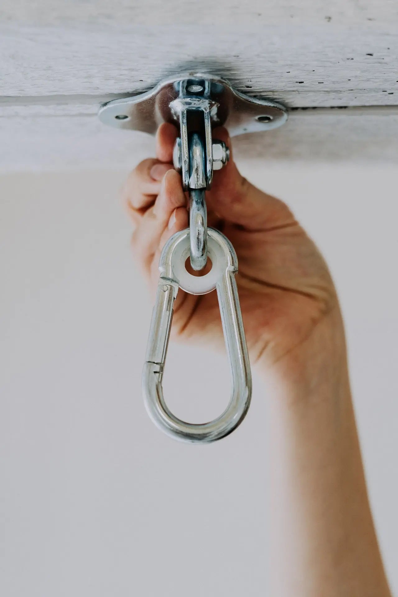 A hand holds a metal hook, ring, chain, and bolt for HopOn Swing Hanger. Concrete ceiling attachment with screws. Suitable for indoor use. Dimensions: 90×168 mm.