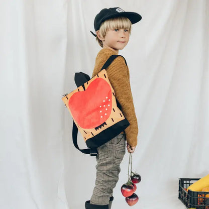 A young boy in a hat and backpack with fruits, showcasing our Kids backpack - Apple. Perfect for outdoor adventures, featuring apple design, velvet top, and waterproof polyester bottom. Ideal for 2-6-year-olds.