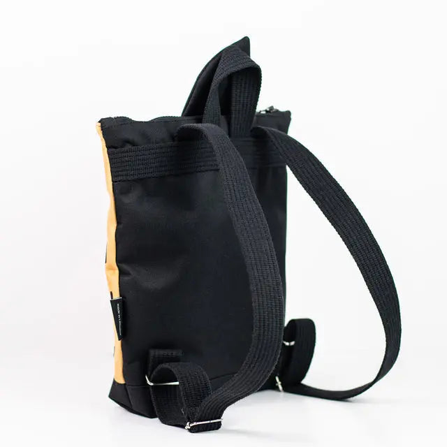 A small kids backpack featuring a black and tan design with apple motif. Made of velvet and waterproof polyester, with adjustable beige shoulder straps and two inside slip pockets.