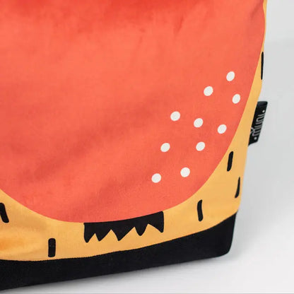 A close-up of a small kids backpack featuring an apple motif. Made of velvet fabric with a waterproof orange bottom. Zipper closure, adjustable shoulder straps, and two inside slip pockets.