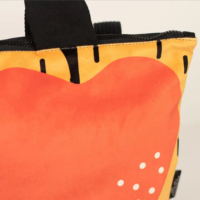 Close-up of a small kids backpack featuring an apple motif. Velvet top with Apple design, waterproof orange bottom, beige shoulder straps, and zipper closure. Ideal for young explorers aged 2-6.