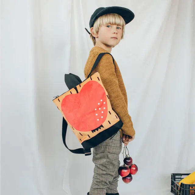 A young boy in a hat and backpack, showcasing our Kids backpack - Apple. Perfect for outdoor adventures, with an apple motif, velvet top, waterproof polyester bottom, and adjustable straps. Ideal for 2-6-year-olds.