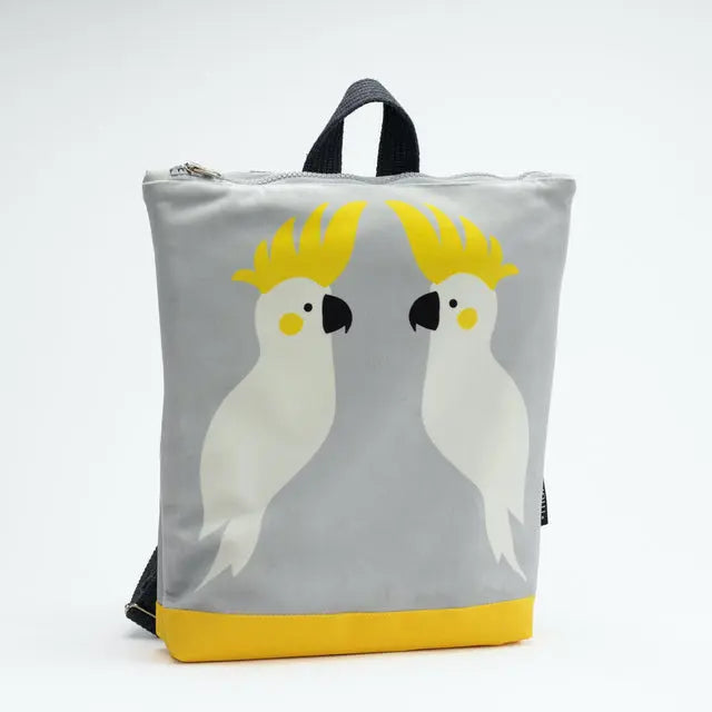 Kids backpack - Cockatoo featuring white birds on grey and yellow bag. Lightweight, adjustable straps, velvet top, waterproof polyester bottom, orange lining. Ideal for 4-10-year-olds. Dimensions: 38cm height, 34cm width.