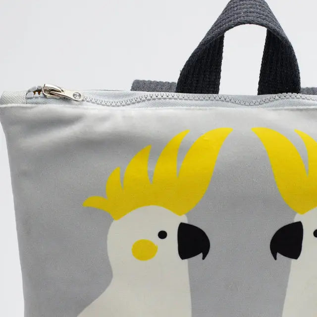 Kids backpack featuring a grey bag with yellow birds, ideal for 4-10-year-olds. Lightweight, adjustable straps, Cockatoo design on velvet top, waterproof polyester bottom, and orange lining. Dimensions: 38cm height, 34cm width.