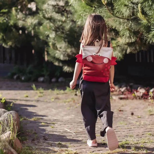 A toddler walks with a CRAB backpack on a path. Velvet top with a Crab design, waterproof polyester bottom, adjustable straps, zipper closure. Two sizes available.