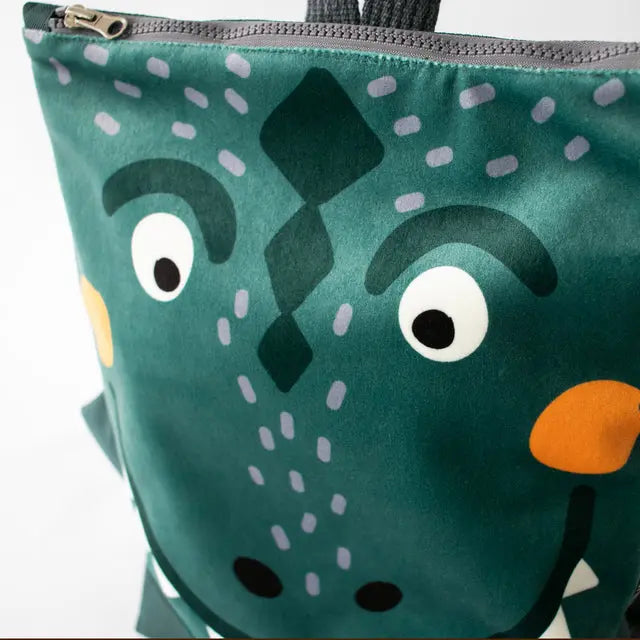 A green kids backpack with a cartoon dinosaur face design, featuring velvet and waterproof polyester materials, adjustable straps, and ample storage space for young adventurers.