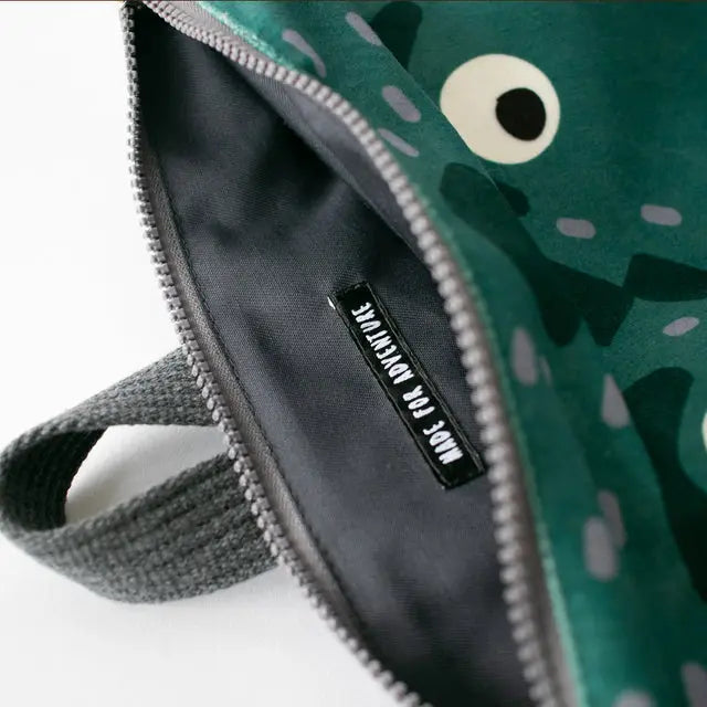 A green kids backpack with a zipper featuring a prehistoric Dinosaur design. Made of velvet and waterproof polyester, with adjustable straps and inside pockets. Sizes: Small (29x26 cm), Large (35x30 cm).