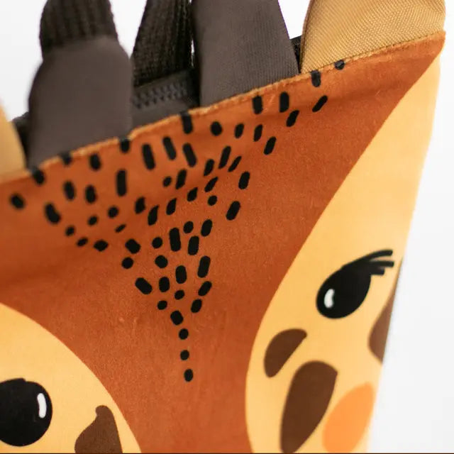 Close-up of a tan giraffe-themed kids backpack with velvet top, waterproof polyester bottom, adjustable beige straps, and zipper closure. Ideal for outdoor adventures.