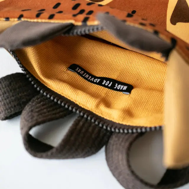 Close-up of a giraffe-themed kids backpack with velvet top, waterproof polyester bottom, and beige shoulder straps. Features zipper closure and two inside slip pockets. Height: 29-35cm, Width: 26-30cm.