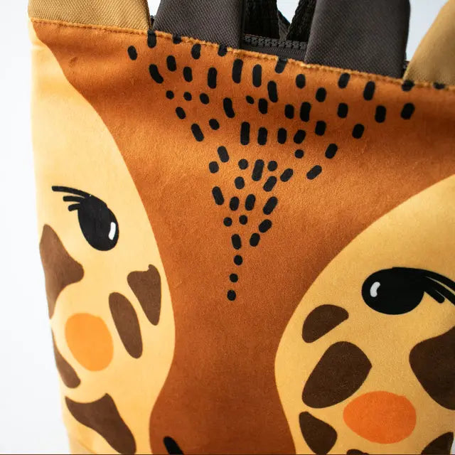 A close-up of a kids backpack featuring a giraffe design. Made of velvet and waterproof polyester, with adjustable shoulder straps and zipper closure. Ideal for outdoor adventures.