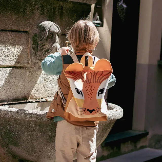 Child wearing a Lion backpack with a face design, khaki pants visible. Functional LINEN backpack for kids, velvet top with lion print, waterproof polyester bottom. Ideal for park trips and playdates.