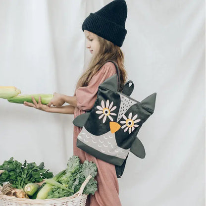 A girl holding a corn cob and a basket of vegetables, showcasing a Kids backpack - Owl. Perfect for adventures, with adjustable straps, velvet top, waterproof polyester bottom, and cute owl design. Dimensions vary.