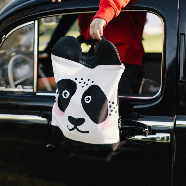 Kids backpack - Panda held by a person in a car window, showcasing its panda face design, perfect for children's outdoor adventures.