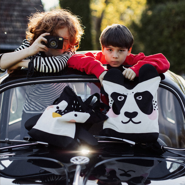 Kids backpack - Panda: Child leans on a panda backpack with a durable design, featuring velvet and polyester materials, perfect for outdoor adventures.