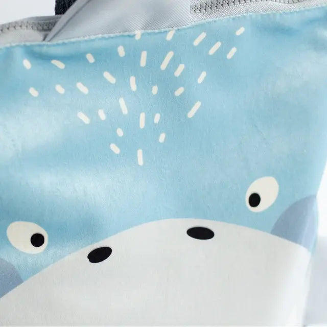 Close-up of a shark-themed kids backpack with velvet top, waterproof polyester bottom, and beige shoulder straps. Features zipper closure and inside slip pockets. Available in small and large sizes.