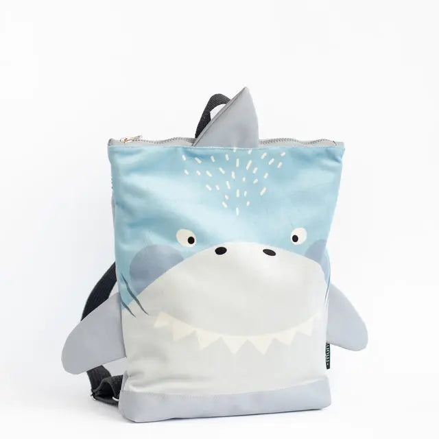 A kids backpack featuring a shark design. Made of velvet fabric with a waterproof polyester bottom. Adjustable shoulder straps and zip closure. Available in small and large sizes.