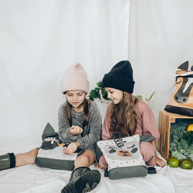 Two girls happily sitting on a bed, one holding a gift. A girl in a hat and sweater, a close-up of a plant, and a pillow with a face on it. A person wearing a pink hat, legs with a bag, and a shoe close-up.