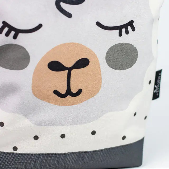 A close-up of a kids backpack featuring a sheep design. Velvet top with Sheep print, waterproof polyester bottom, adjustable beige shoulder straps, zipper closure, and two inside pockets.